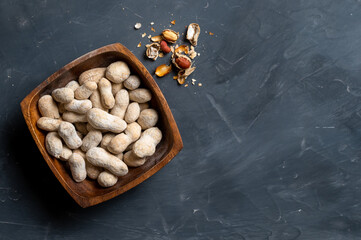 Peanuts in wooden bowl and scattered peanuts on table surface, top view. Copy space.