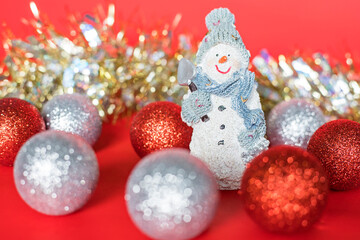 Fototapeta na wymiar Christmas and new year tree decorations. Christmas composition of little snowman, silver and red balls and glitter garland on red background.