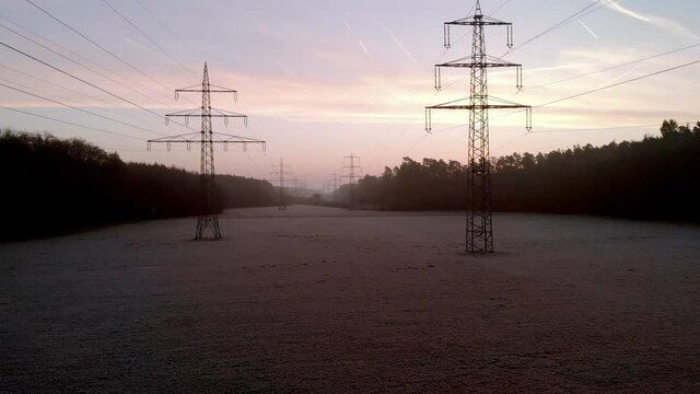 Slow rise up fly backwards crane shot revealing a panoramic view of High-voltage line in foggy forest strip, in early morning misty light