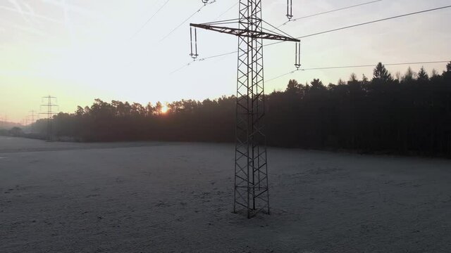 Rise up aerial shot of high voltage power line electric pole, amidst foggy forest, revealing a majestic golden sunrise