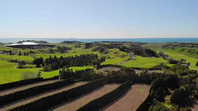 Backward aerial over lush farmland on green coast of North Island of New Zealand