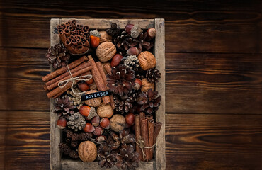 cones, nuts, cinnamon sticks in box on old wooden background. november. seasonal late autumn background. fall time. organic nature product