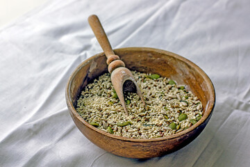 Cereal mixture of sesame seeds, pumpkin seeds, sunflower seeds in a wooden bowl with a scoop. A mixture of seeds for baking sprinkling bread on a white background. Natural food concept
