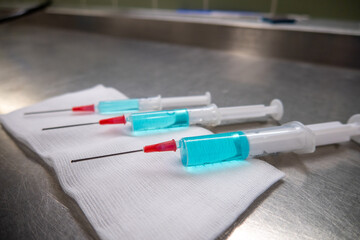 3 differently sized syringes filled with blue liquid lie on a white compress