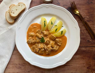 Traditional Hungarian chicken goulash, also known as chicken paprikash, or paprika chicken, in juicy paprika sour cream sauce and served with boiled potatoes.