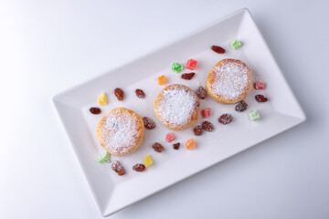 Curd pancakes with raisins and candied fruits on a white plate, top view