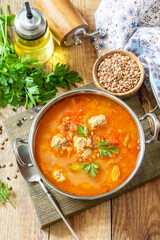 Tomato lentil soup with meatballs and vegetables on a wooden table.