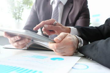 Two businessman are looking and studying statistics on tablet display closeup. Male hand opponent...