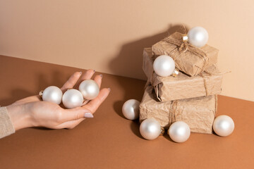 The woman hand with white christmas balls is near the paper gift boxes with rope. Holiday concept. Idea for decoration presents. Top view.