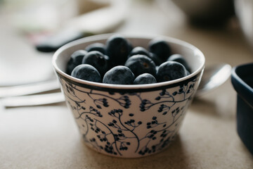A cup of blueberries is on the table in the kitchen.