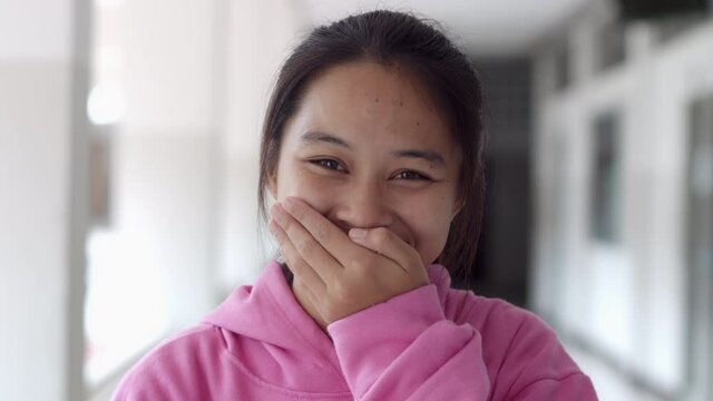 A female teenage Asian high school student girl in a pink sweater is laughing and embarrassed that she covers her mouth.