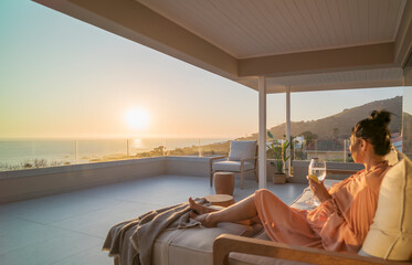 Woman enjoying white wine and sunset ocean view on luxury balcony
