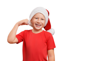 Cheerful happy caucasian boy wearing a red t-shirt laughing and looking at the camera putting on a handmade knitted Santa hat isolated on white background with copy space.