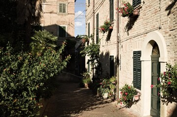 An alley of a medieval Italian village with brick houses, plants and flowers (Corinaldo, Marche, Italy)