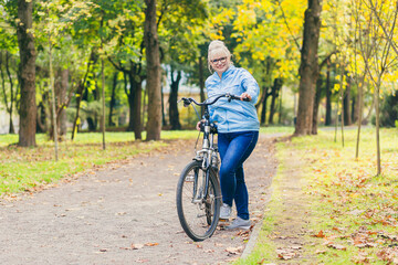Naklejka premium senior woman walking in the park with a bicycle, sunny day