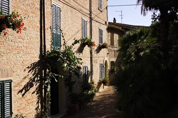 Fototapeta na wymiar An alley of a medieval Italian village with brick houses, plants and flowers (Corinaldo, Marche, Italy)
