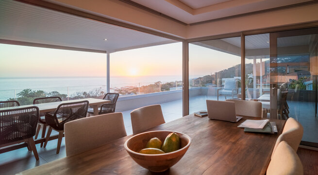 Laptop on luxury dining table with scenic ocean view at sunset