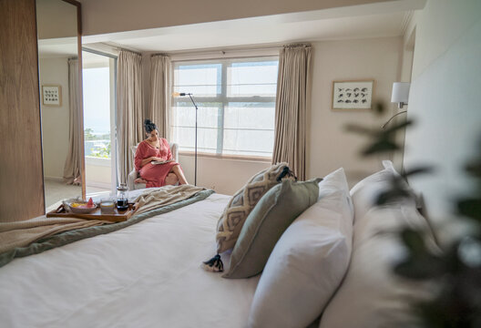Woman reading book at sunny morning window in luxury master bedroom