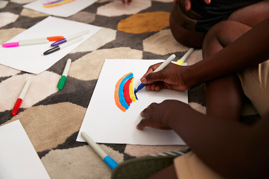 Boy drawing multicolor rainbow with markers on rug
