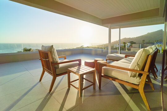 Sofa and armchair on sunny tranquil luxury patio with ocean view