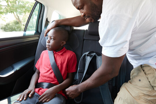 Father fastening seat belt for son in back seat of car
