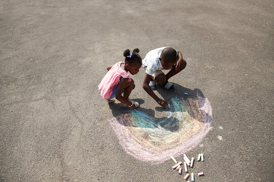 Brother and sister drawing rainbow with sidewalk chalk on pavement