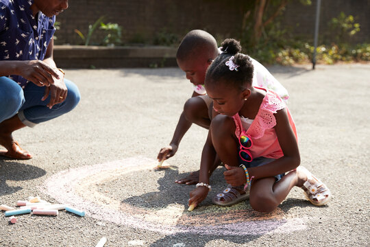 Brother and sister coloring rainbow with chalk on sunny sidewalk