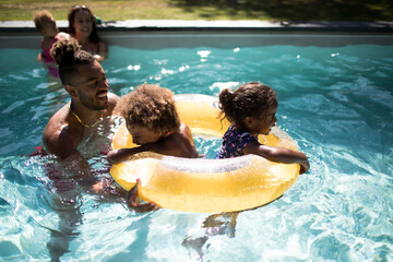 Family playing with inflatable ring in sunny summer swimming pool