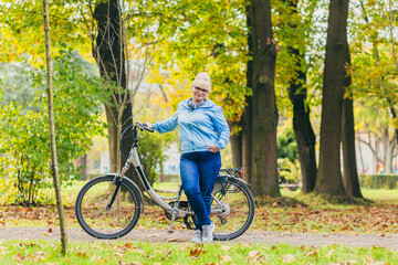 Obraz premium senior woman walking in the park with a bicycle, sunny day
