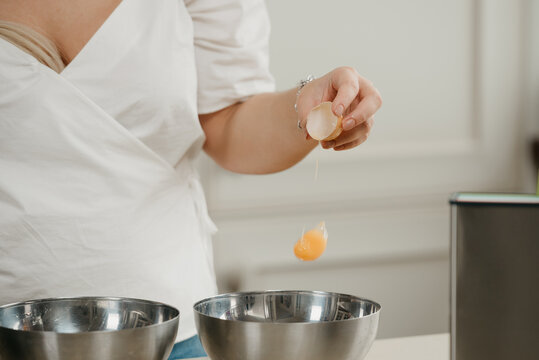 A photo of the hand of a woman who is dropping the yolk of the organic farm egg to the stainless steel soup bowl in a kitchen. A falling yolk.
