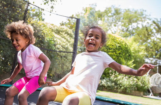 Portrait happy playful sisters jumping on backyard trampoline