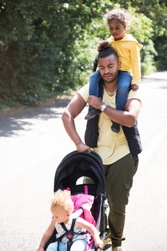 Father carrying and pushing daughter in stroller on sunny path