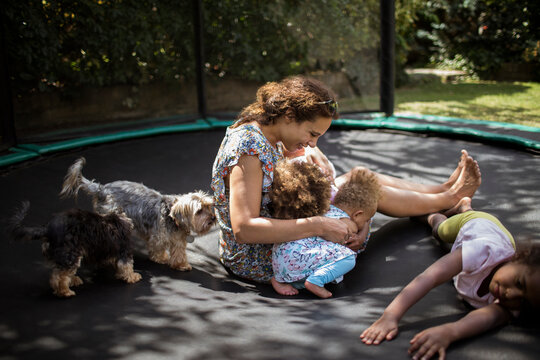Mother and daughters playing on backyard trampoline with dogs
