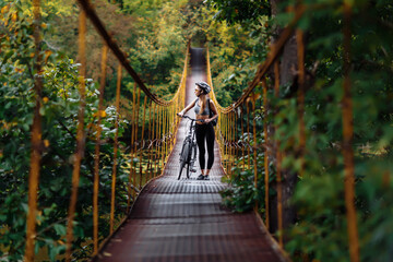 Fit young woman wearing sportswear with her bicycle on suspension bridge at autumn