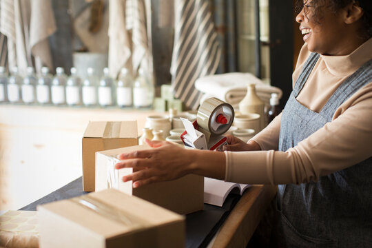 Happy female shop owner taping e-commerce packages