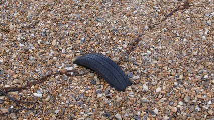Tyre anchoring rusty chain on shingle beach for use as background