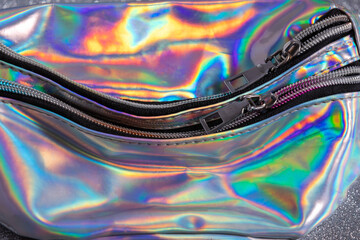 Selected focus of Zipper on a neon holographic color bag on the bokeh silver background.
