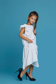 Cute Little Child Girl In White Oversized Dress And Shoes On Blue Background. Child Playing Grown Ups