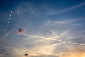 A serene evening sky with contrails forming a cross pattern at sunset, highlighted by pink clouds and a tranquil atmosphere, showcasing nature's beauty. represent tranquility, aviation, evening skies