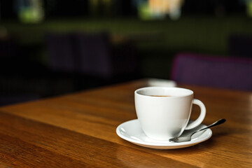 A white cup of black coffee, white saucer, spoon, wooden table, at a cafe