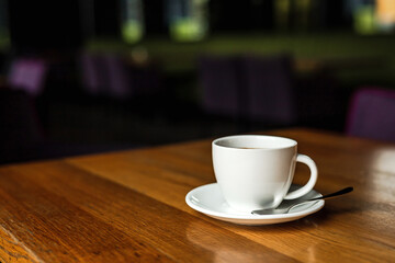 A white cup of black coffee, white saucer, spoon, wooden table, at a cafe
