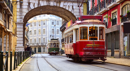 Lisbon, Portugal. Vintage red retro tram on narrow bystreet tramline in Alfama district of old town. Popular touristic attraction of Lisboa city. Public tramways trasport. - obrazy, fototapety, plakaty