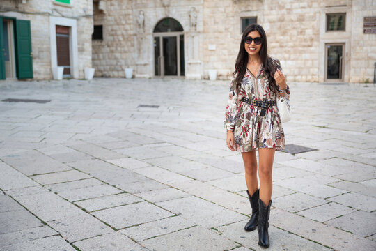 Fototapeta Outdoors, evening, young brunette Italian woman and long hair with flowered dress walks in the narrow streets of a touristic town of Molfetta in Puglia, Italy