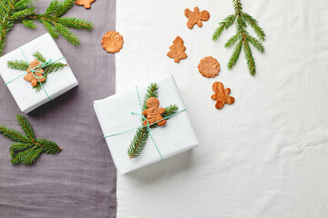 Christmas gifts wrapped in white paper and decorated with spruce sprigs and gingerbread cookies