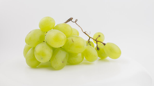 Fresh bunch of juicy grapes rotate on a white background. Ripe juicy grapes rotate on a plate. Close-up of a bunch of white grapes.
