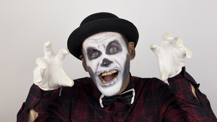 A horrible man in clown makeup grimaces and makes frightening gestures. A scary clown looks at the camera and laughs terribly. Scary grimaces of a clown looking at the camera.