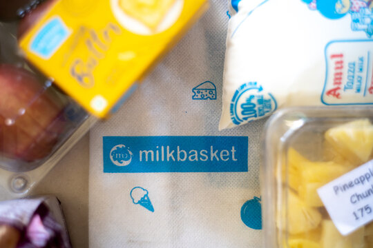 Flatlay image of multiple home essentials like milk, butter, fruits and bread coming from a milkbasket bag which provides a daily subscription delivery of groceries