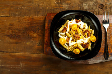 Pasta with chicken and cheese in a black plate on a table on a wooden stand with a fork.