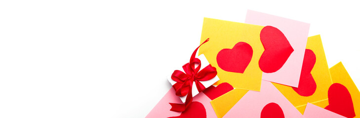 valentines day. gift box with red bow and blank sheet with cut paper hearts for love message on a white background. banner