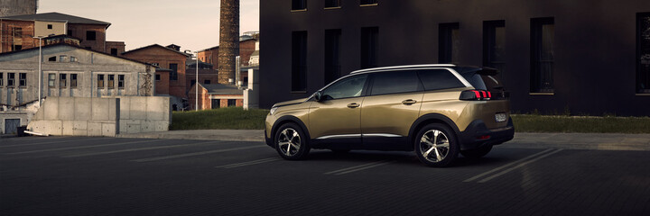 Katowice/Poland - 06.03.2017: Golden Peugeot 5008, seven-person SUV, in the parking lot under a modern black office building Porcelana Slaska Park. In the back you can see the old factory buildings